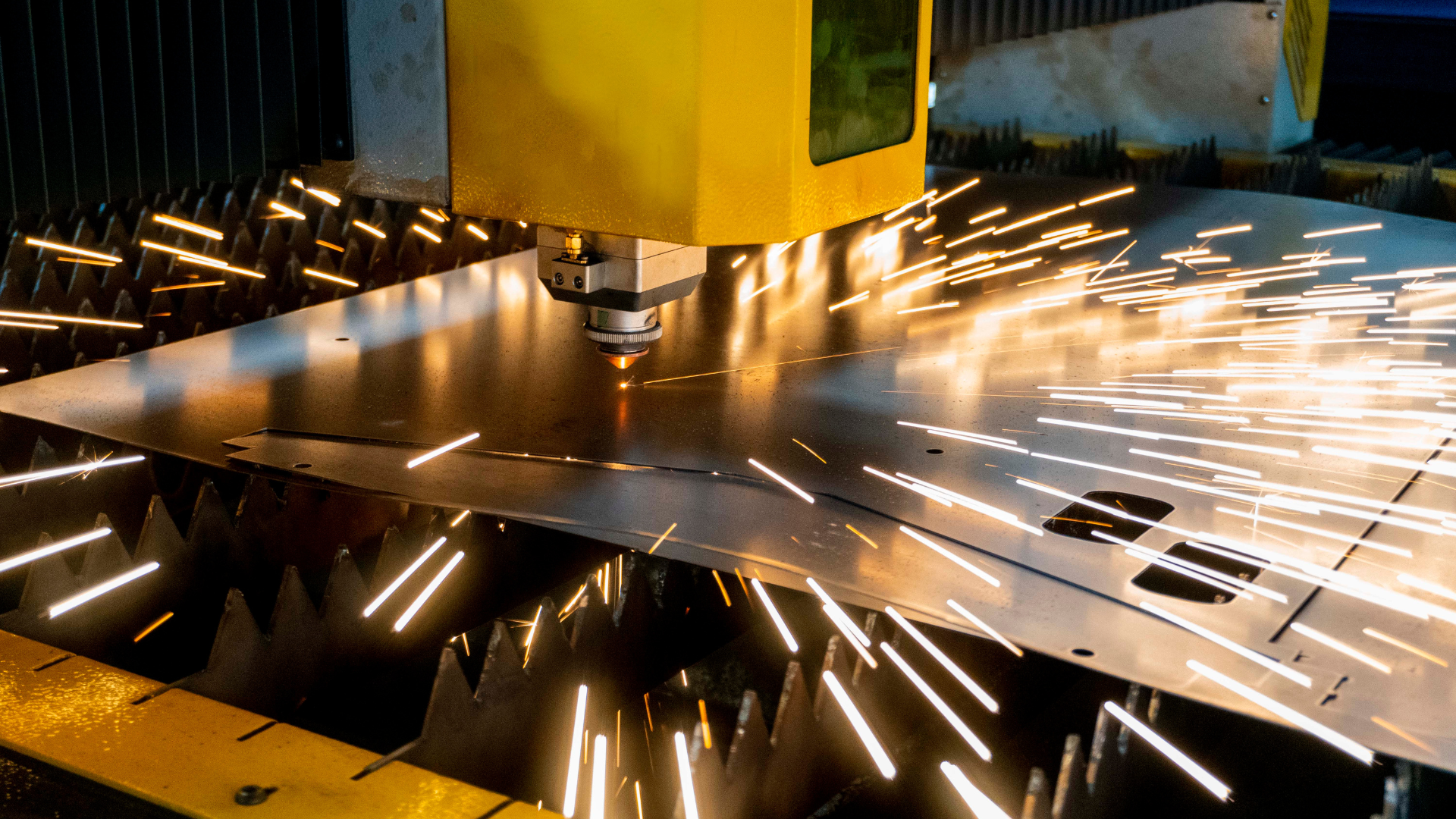 Laser cutting machine in operation, producing sparks while cutting a metal sheet.